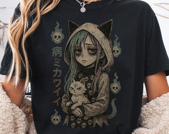 May include: Black t-shirt with a graphic print of a girl with blue hair and cat ears holding a white cat. The girl is wearing a hooded sweatshirt with a skull pattern. The text "病みかわいい" is printed on the shirt.