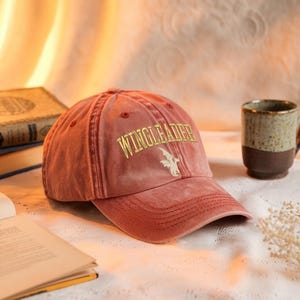 以下が含まれることがあります： 黒い持ち手と「But First, Coffee」のテキストが黒い太字で書かれた白いセラミックマグ。マグカップはぼやけた背景に置かれており、居心地の良い環境を示唆しています。