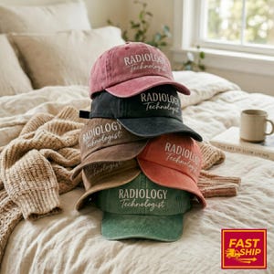 Peut inclure: Une pile de six casquettes de baseball de différentes couleurs, dont rose poudré, noir, marron, orange et vert. Chaque casquette porte l'inscription blanche "RADIOLOGY Technologist". Les casquettes sont empilées sur un lit.