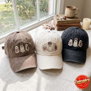 May include: Three baseball caps in brown, cream, and black, each featuring an embroidered design of three ghosts reading books. The ghosts are depicted in white with brown outlines, holding open books, with one ghost balancing a stack of books on its head.