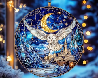 Puede incluir: Adorno redondo de vidriera con un búho nival con las alas extendidas, una luna creciente y un castillo. El adorno tiene un marco dorado y un lazo para colgar. El fondo es un paisaje invernal con un cielo estrellado.