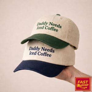 Puede incluir: Dos gorras de béisbol apiladas una encima de la otra. Las gorras son de color beige con una visera verde oscuro y azul marino. El texto "Daddy Needs Iced Coffee" está bordado en la parte delantera de cada gorra en verde oscuro y azul marino.