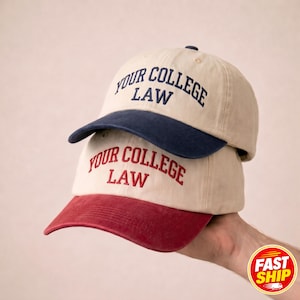 Peut inclure: Deux casquettes de baseball empilées verticalement. La casquette supérieure est beige avec une visière bleu marine et le texte YOUR COLLEGE LAW brodé en bleu marine. La casquette inférieure est beige avec une visière bordeaux et le texte YOUR COLLEGE LAW brodé en bordeaux.