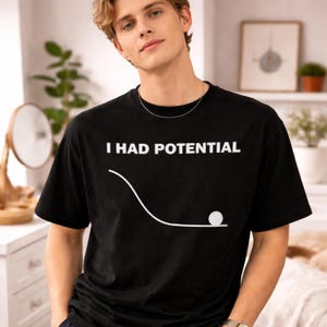 Puede incluir: Camiseta negra con el texto blanco "I HAD POTENTIAL" sobre una línea blanca y un gráfico de bola blanca. La camiseta es de cuello redondo y manga corta.
