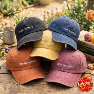 May include: A collection of five baseball caps in charcoal, blue, yellow, orange, and maroon, each featuring the embroidered white text "truth matters" on the front panel. The caps have a distressed, washed-out fabric finish and a curved brim.