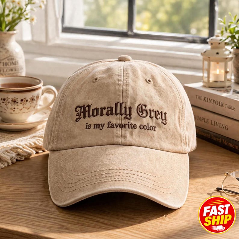 May include: A beige baseball cap with a distressed, washed-out texture. The front features dark brown embroidered text that reads Morally Grey is my favorite color in a decorative, serif font. The cap has a curved brim and a button on top.