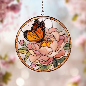 Può includere: Vetrata rotonda raffigurante una farfalla con ali arancioni e nere posata su un fiore di peonia rosa. L'opera è incorniciata in metallo color bronzo e appesa a una catena.