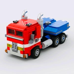 Könnte beinhalten: Ein roter, weißer und blauer Spielzeug-LKW aus ineinandergreifenden Kunststoffbausteinen. Der LKW hat ein rotes Fahrerhaus mit silbernen Auspuffrohren und einen blauen Anhänger. Der Spielzeug-LKW hat schwarze Räder, vor weißem Hintergrund.