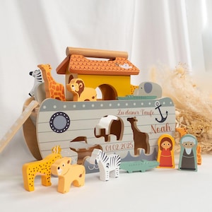 Könnte beinhalten: Ein Holzspielzeug, die Arche Noah, mit gelbem Dach und hellgrauem Rumpf. Die Arche hat eine Rampe und enthält Tierfiguren wie Giraffe, Löwe, Zebra und Elefant. Der Name "Noah" und das Datum "01.02.2025" sind auf der Seite zu sehen.