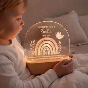Könnte beinhalten: Personalisiertes Nachtlicht mit Regenbogen-Design. Das Licht ist mit dem Namen "Emilia" und dem Datum "13.06.2026" graviert. Es hat einen Holzsockel und eine transparente Acrylplatte mit Regenbogen, Taube und floralem Design.