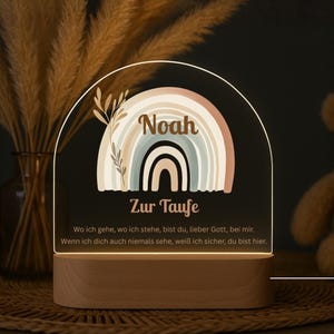 Könnte beinhalten: Nachtlicht mit Holzsockel und klarer Acrylplatte. Die Platte zeigt ein Regenbogen-Design, den Namen "Noah" und den Text "Zur Taufe". Ein religiöses Zitat ist ebenfalls sichtbar. Das Licht strahlt warm.