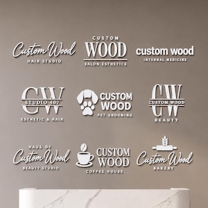 May include: A collection of nine white 3D wall-mounted business logos featuring various designs and text including Custom Wood Hair Studio, Salon Esthetics, Internal Medicine, Studio 407, Pet Grooming, Beauty, Coffee House, and Bakery above a marble desk.
