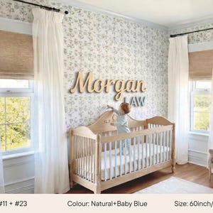 May include: A nursery with a wooden crib and a beige armchair. The wall features a floral wallpaper and a wooden name sign that reads "Morgan LAW". The crib is 60 inches (150 cm) long and has a baby blue mattress. White curtains frame the windows.