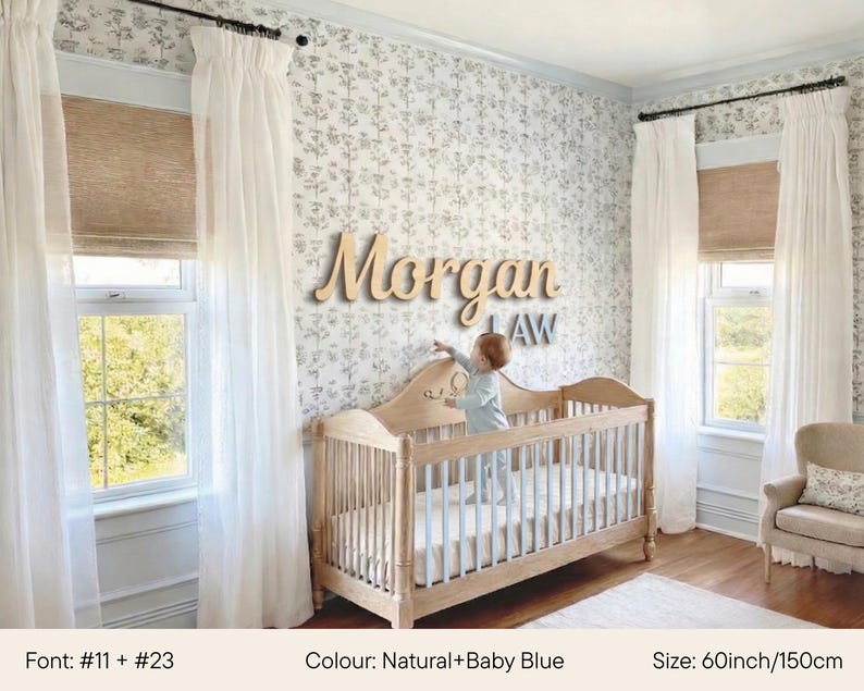 May include: A nursery with a wooden crib and a beige armchair. The wall features a floral wallpaper and a wooden name sign that reads "Morgan LAW". The crib is 60 inches (150 cm) long and has a baby blue mattress. White curtains frame the windows.