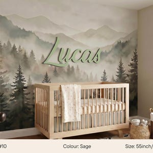 May include: A nursery with a light wood crib and a wall mural depicting a misty forest and mountains. The name "Lucas" is displayed in sage green script. The crib is 55 inches wide.