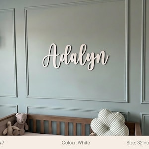 May include: White wooden name "Adalyn" in a cursive font, mounted on a light blue wall. The name is 32 inches (80cm) wide. A crib with stuffed animals and a cloud-shaped pillow are in the foreground.