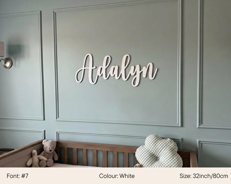 May include: White wooden name "Adalyn" in a cursive font, mounted on a light blue wall. The name is 32 inches (80cm) wide. A crib with stuffed animals and a cloud-shaped pillow are in the foreground.
