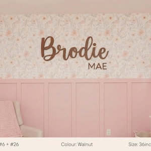 May include: A walnut-colored wooden sign with the name "Brodie" and the name "MAE" below it. The sign is 36 inches (92cm) wide and is displayed on a pink wall with floral wallpaper.
