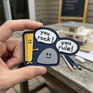 May include: A navy blue and gray patch with a yellow ruler and a gray rock, both with smiling faces. The patch has speech bubbles that say "You rock!" and "You rule!"