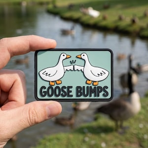 May include: A rectangular patch with a black border and a light teal background. The patch features two white cartoon geese bumping beaks, with the words "GOOSE BUMPS" in black block letters below the geese.