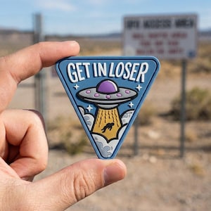 May include: A blue triangular patch with the text "GET IN LOSER" and an illustration of a UFO abducting a person. The UFO is purple and gray, with a yellow beam. The patch has a white border and star accents.