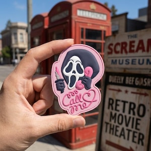 May include: A pink and black patch featuring the Ghostface mask from the Scream movie franchise. The patch shows Ghostface holding a knife and a pink telephone, with the words "Call Me" in a heart-shaped design.