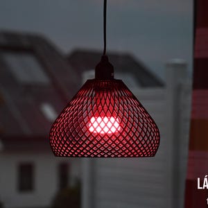 Può includere: Una lampada a sospensione rossa con un paralume a motivo di diamanti, illuminata da una lampadina brillante. La lampada è appesa a un cavo nero. Il testo "LÁMPARA de techo" è visibile.