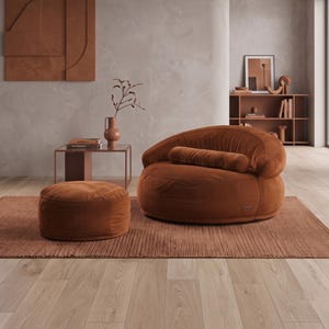 May include: A round, rust-colored corduroy armchair with a matching cylindrical bolster pillow and a circular ottoman. The furniture set is placed on a rectangular, textured rug in a room with light wood flooring and neutral walls.