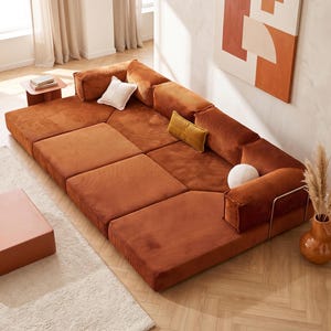 May include: A large, modular floor sofa upholstered in rust-colored corduroy fabric. The sofa features a low-profile design with multiple rectangular seat sections, back cushions, and armrests. It includes one white square pillow and one yellow rectangular pillow.