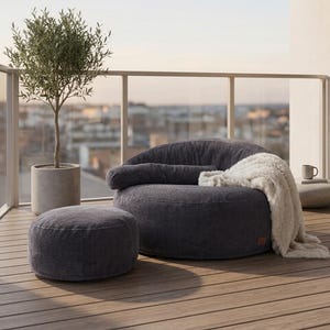 May include: A dark gray corduroy circular lounge chair with a matching cylindrical ottoman. The chair features a low profile, a rounded backrest, and a soft white faux fur throw blanket draped over the side, creating a cozy seating arrangement.
