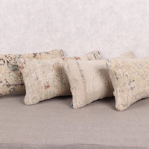 May include: Four rectangular cushions with a vintage, textured look. The cushions are mainly beige with faded patterns in muted colours such as red, blue, and green. They are arranged side by side on a neutral surface.