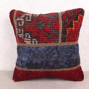 May include: Square decorative pillow with a patchwork design. The pillow features a combination of red, blue, and brown colors. The top section has a red background with a geometric pattern. A blue band is in the middle, and the bottom is red.