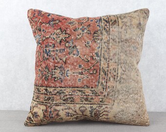 May include: Square cushion with a vintage rug design. The cushion features a patchwork design with a red and beige colour scheme, with intricate floral and geometric patterns. The cushion is a home decor item.
