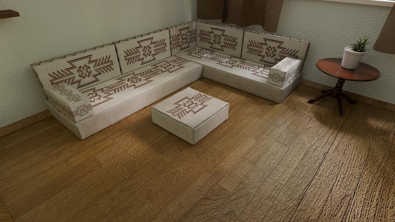 May include: A beige sectional sofa and matching ottoman with brown geometric patterns. The sofa is arranged in an L-shape, with a small round side table and a potted plant nearby. The floor is made of wood.