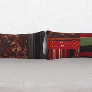 Könnte beinhalten: Zwei rechteckige Kissen mit Patchwork-Designs. Ein Kissen hat orange, braune und schwarze Muster. Das andere Kissen hat rote, grüne und schwarze Abschnitte. Beide Kissen liegen auf einer neutralen Oberfläche, etwa 60 cm lang.