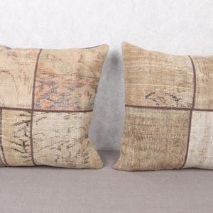 May include: Two square throw pillows with a patchwork design. The pillows are in shades of beige and brown, with a distressed, vintage look. Each pillow is divided into four sections with dark brown stitching.