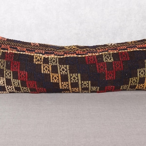 May include: Rectangular decorative pillow with a dark brown background and a geometric pattern in red, yellow, and white. The pillow has a woven texture and a patterned border.