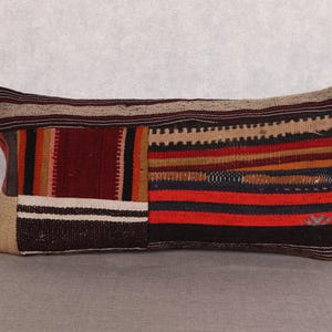 Puede incluir: Cojín rectangular con diseño patchwork. El cojín presenta una mezcla de colores, incluyendo rojo, marrón, beige y negro. El diseño incorpora rayas y patrones geométricos, creando una apariencia texturizada. El cojín probablemente está hecho de tela tejida.