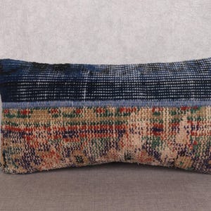 May include: Rectangular decorative pillow with a patchwork design. The top section is dark blue, the middle section is a light blue, and the bottom section is a mix of beige, red, green, and blue. The pillow is placed on a gray surface.