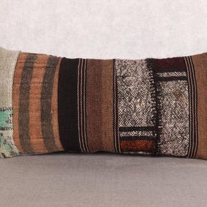 May include: Rectangular decorative pillow with a patchwork design. The pillow features a mix of brown, black, and beige tones with striped and textured patterns. The left side has a section of light green and blue accents.