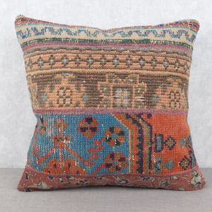 May include: Square decorative pillow with a patchwork design. The pillow features a mix of colors including blue, orange, brown, and red. The design incorporates geometric and floral patterns, creating a vintage or bohemian aesthetic.