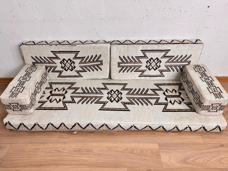 May include: A cream-colored, modular sofa with geometric patterns in brown. The sofa includes a base, two back cushions, and two armrests. The design features repeating geometric shapes and a zig-zag border along the base.