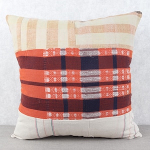 May include: Square decorative pillow with a patchwork design. The top section features cream and tan stripes, transitioning to a bold orange and burgundy plaid pattern in the center. The bottom section has a cream base with thin blue stripes.