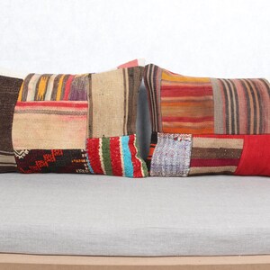 May include: Two rectangular patchwork cushions with a variety of colours and patterns. The cushions feature a mix of brown, red, beige, and colourful striped fabric pieces. They are placed on a light grey surface.