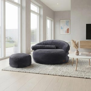 May include: A dark gray corduroy bean bag chair with a matching round ottoman. The chair features a low-profile, rounded silhouette with a horizontal bolster cushion across the backrest, providing a soft, textured seating option for a living space.