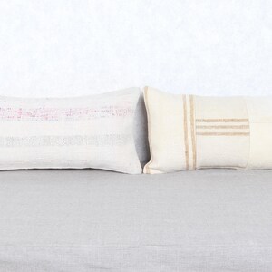 May include: Two rectangular throw pillows. One is off-white with pink and purple stripes. The other is off-white with tan stripes and patches. Both pillows are on a gray surface.