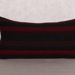May include: Rectangular pillow with horizontal stripes in shades of black, burgundy, and brown. The pillow has a textured appearance and is likely made of woven fabric. The design is simple and could complement various decor styles.