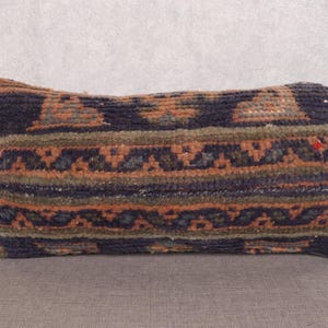 May include: Rectangular pillow with a woven design in shades of navy blue, orange, and olive green. The pillow features a geometric pattern and a textured surface, suitable for home decor.