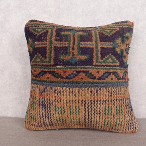 May include: Square decorative pillow with a geometric pattern in shades of navy, green, and orange. The pillow has a textured appearance, with a woven design. The pillow is a square shape, suitable for a sofa or bed.