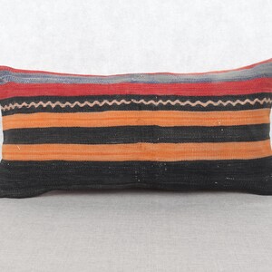 May include: Rectangular cushion with a striped pattern in red, orange, black, and grey. The cushion features a zig-zag design in white. Suitable for a sofa or bed.